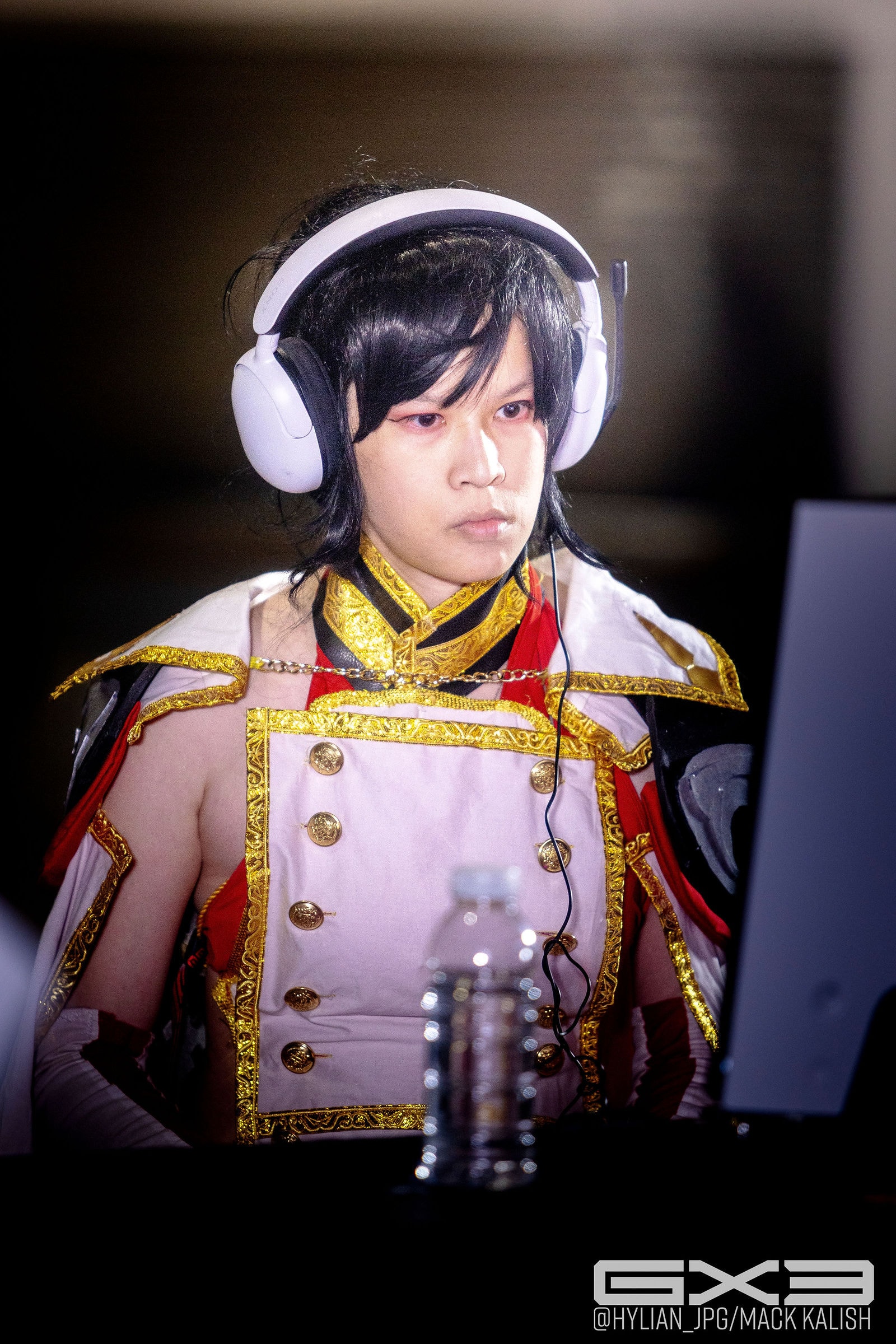 A competitor in a pink and gold costume focuses on a monitor while wearing headphones at GENESIS X3