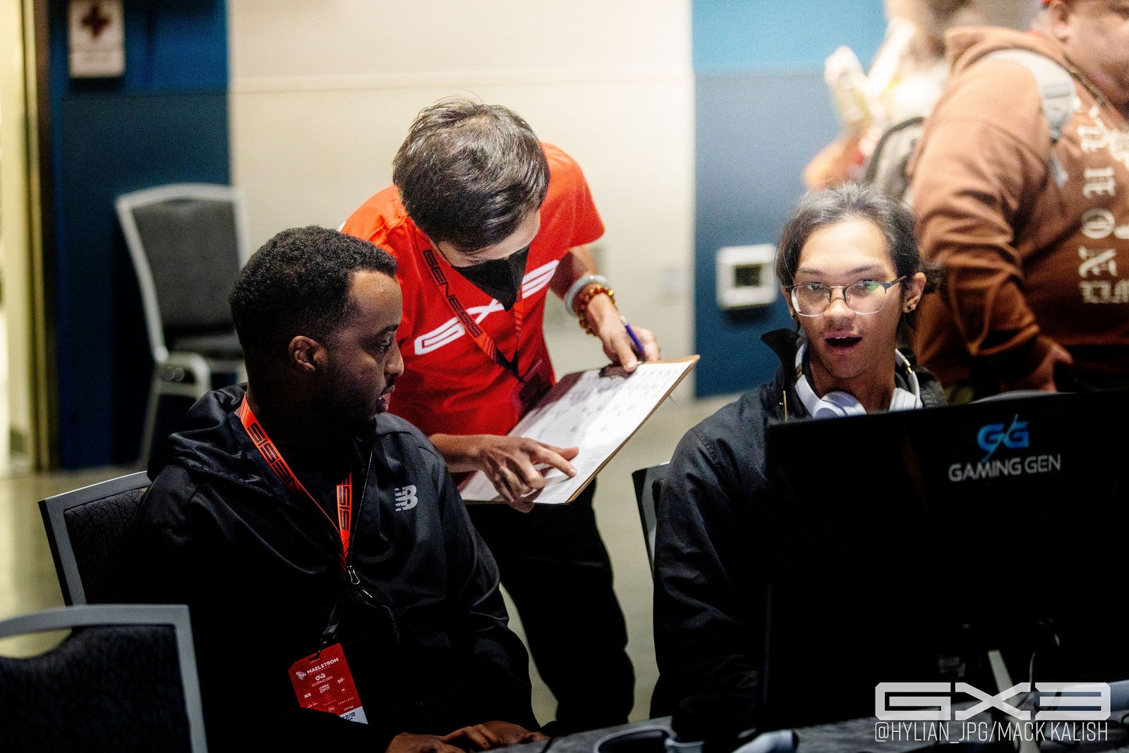 A volunteer assists competitors at a GENESIS X3 tournament station